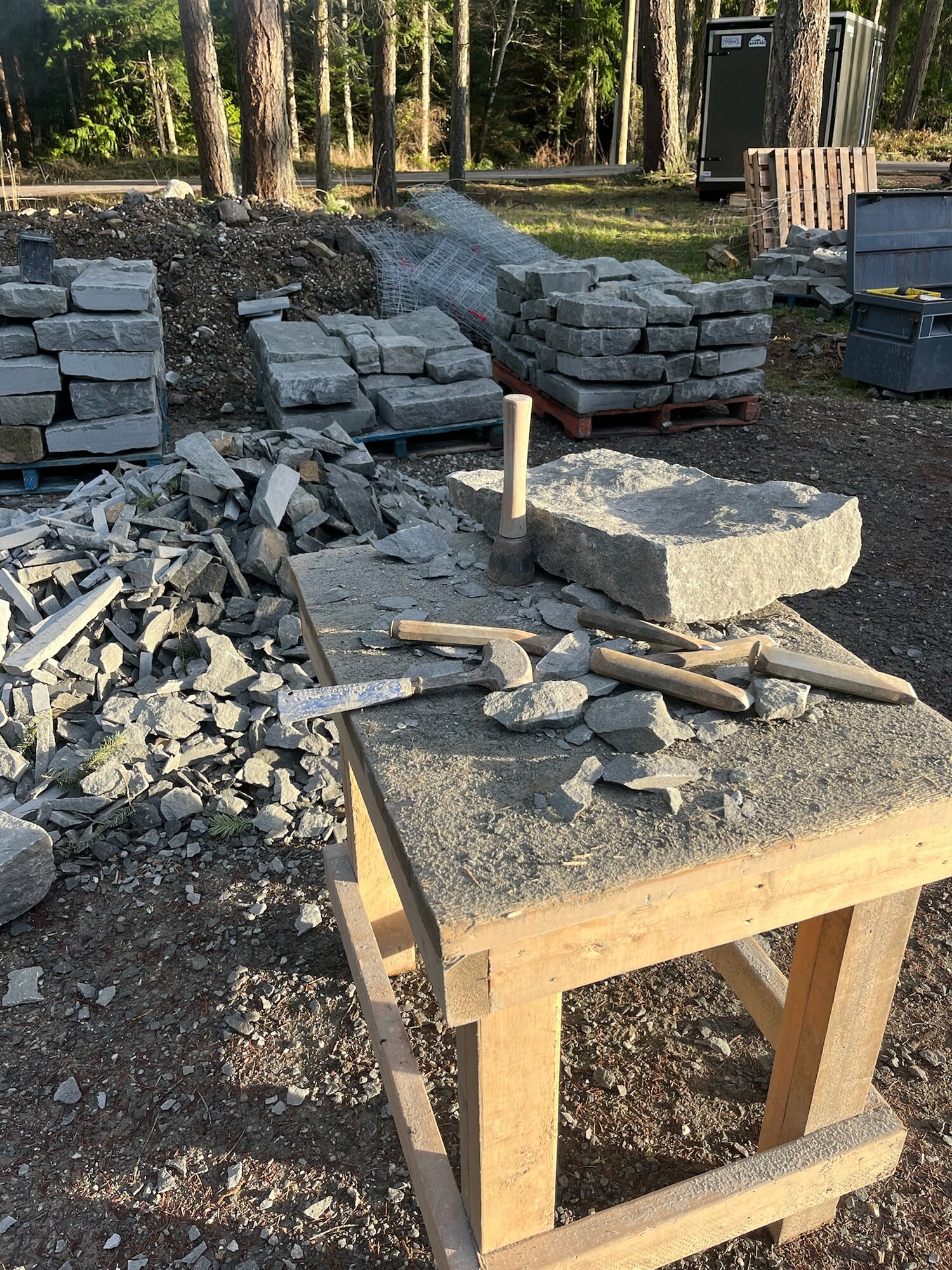 Stone-cutting workbench with chisels and hammers, stone pallets in background