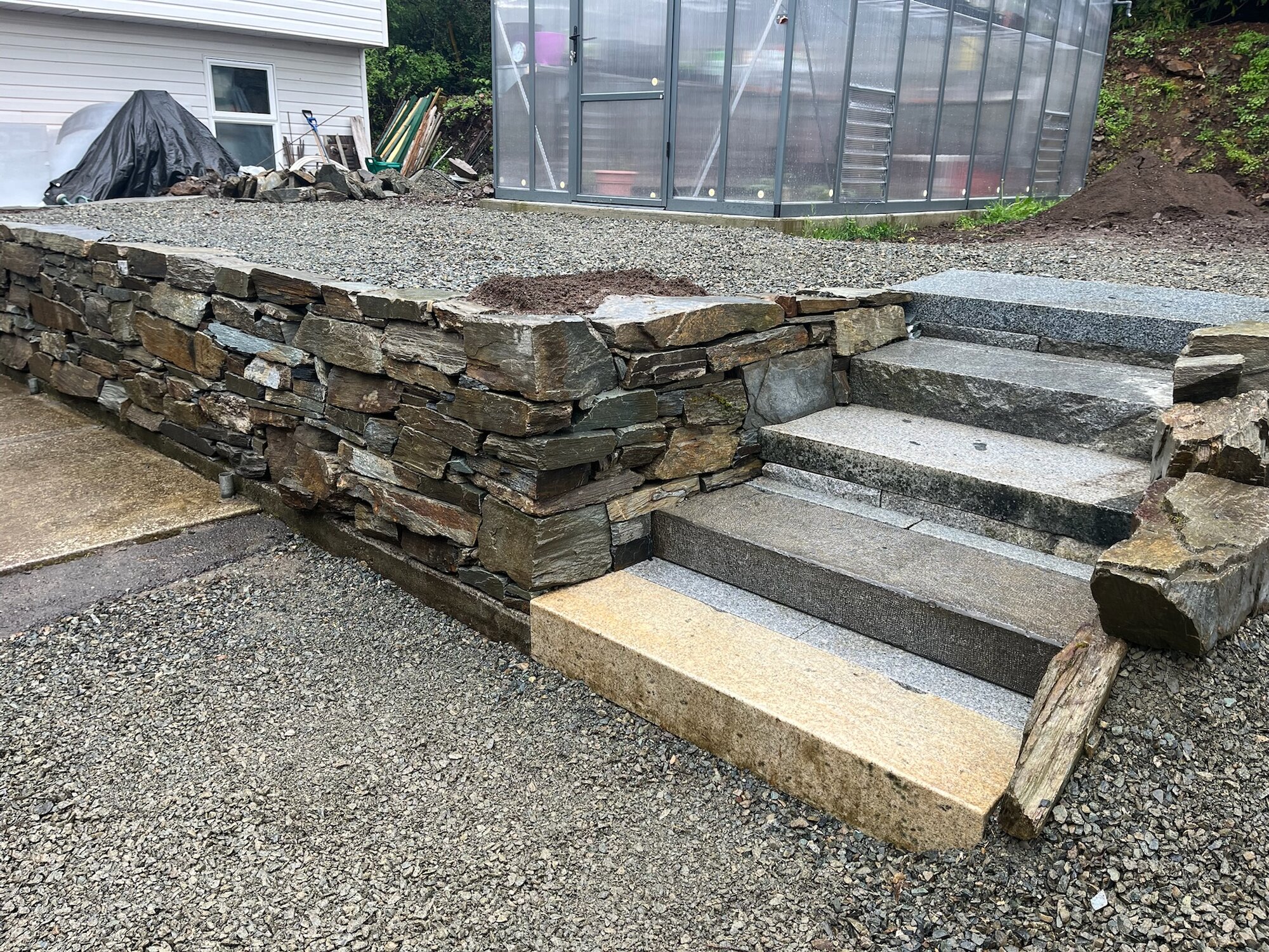 Dry-stack retaining wall with granite steps beside a greenhouse