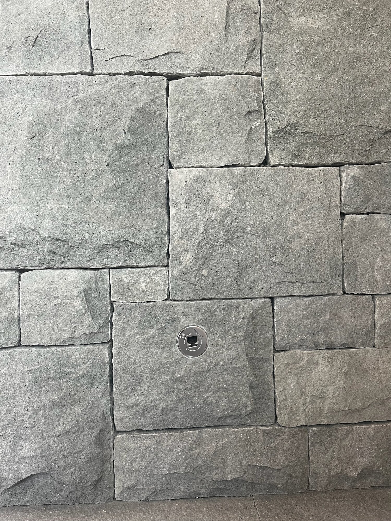 Large-format grey granite ashlar wall with a flush-mounted electrical outlet